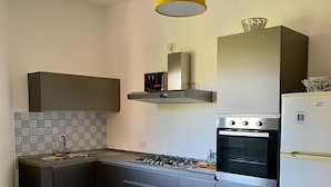 A modern kitchen with grey cabinets, a white countertop, a gas stove, a built-in oven, and a white refrigerator. - Apartment with Garden View (Lecce)