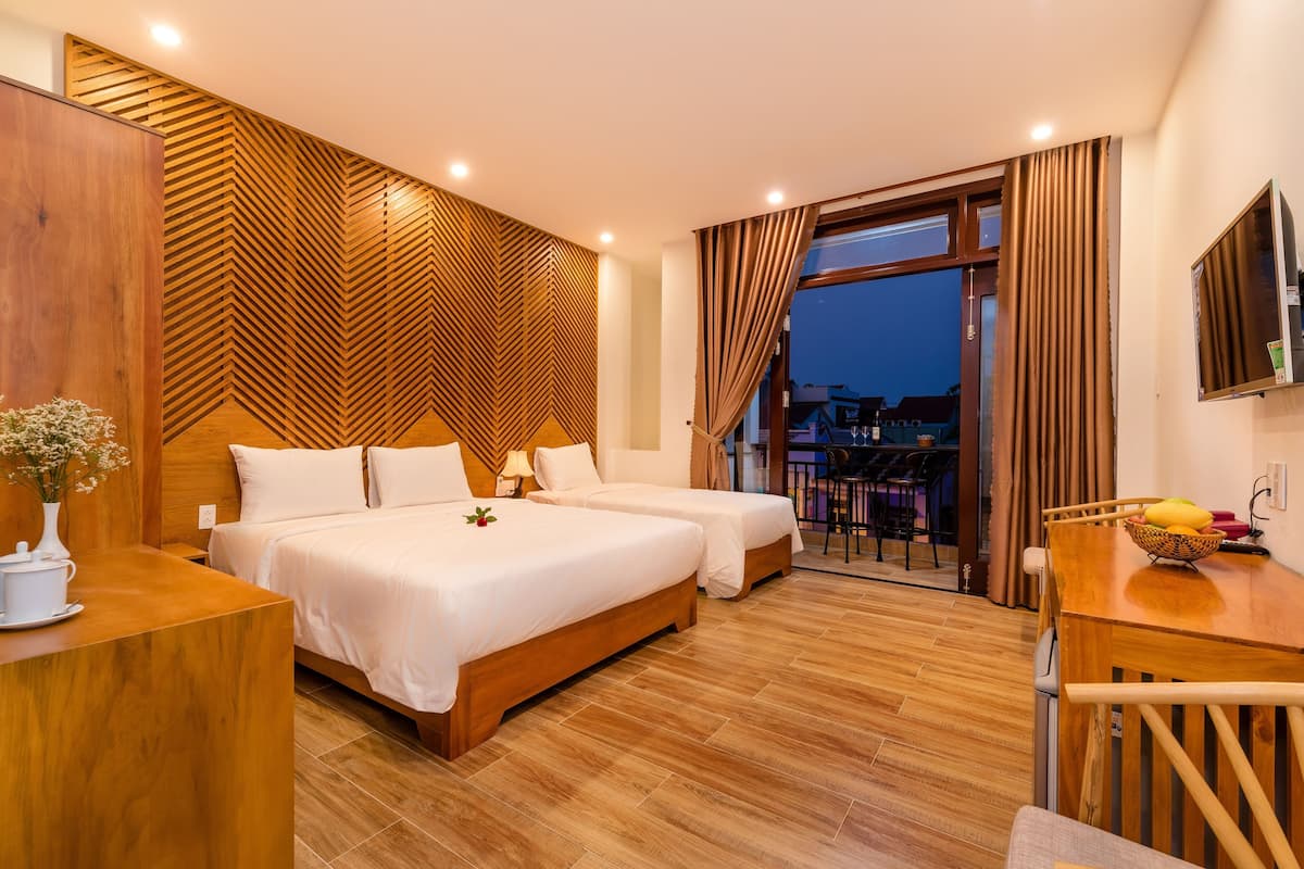 A hotel room with two beds, a wooden headboard, a desk, and a balcony with a view of buildings.