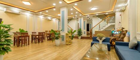 A spacious lobby with a wooden floor, a reception desk, a staircase, and seating areas.