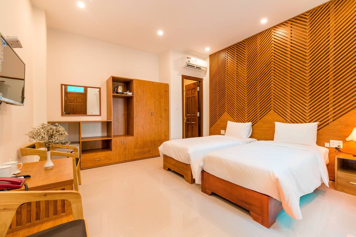 A modern bedroom with two beds, wooden furniture, a desk, and a mirror.