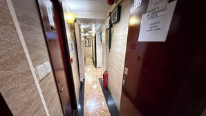 Un couloir d’hôtel avec un sol en marbre, des portes et un extincteur.
