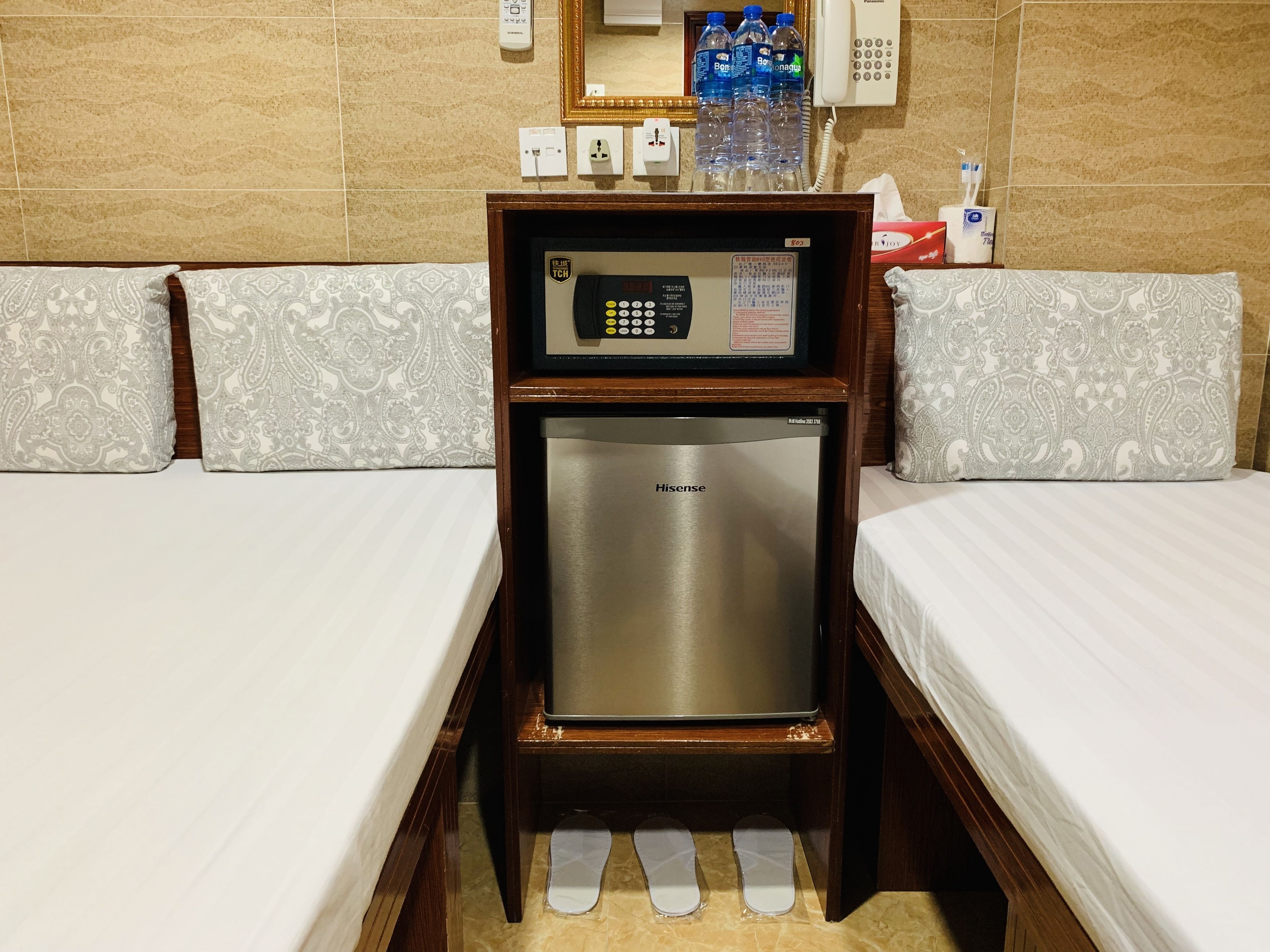 A compact hotel room with two beds, a minibar, a small refrigerator, and a bedside telephone.