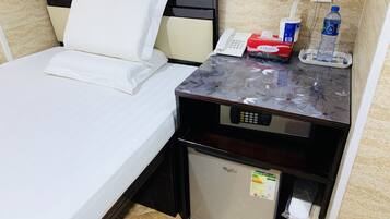A hotel room with a bed, a bedside table with a phone, a tissue box, a water bottle, and a small refrigerator.