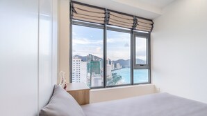 Habitación de hotel con una ventana grande, una cama y vistas a la ciudad y la playa.