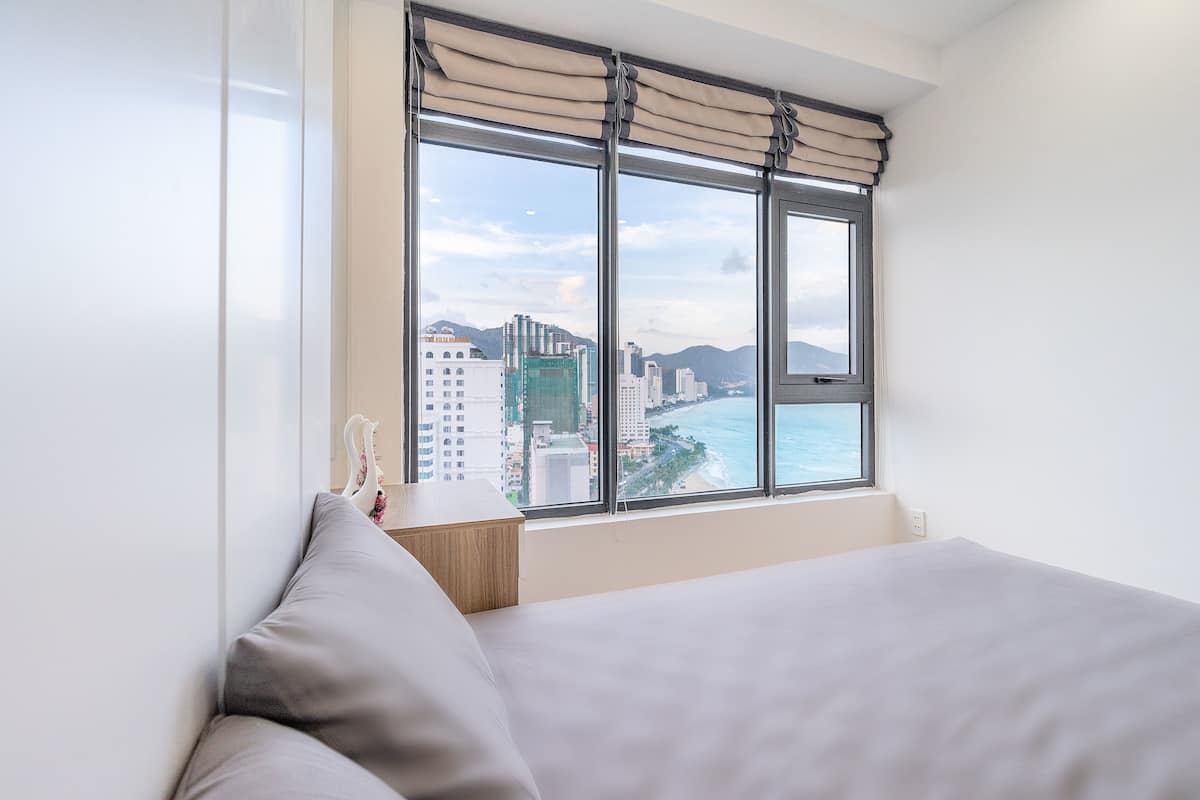 Ein Hotelzimmer mit großem Fenster, einem Bett und Blick auf Stadt und Strand.