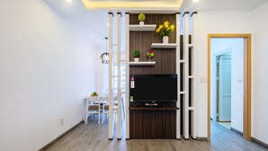 Una sala de estar moderna con un televisor de pantalla plana, piso de madera, muebles blancos y objetos decorativos en estanterías.