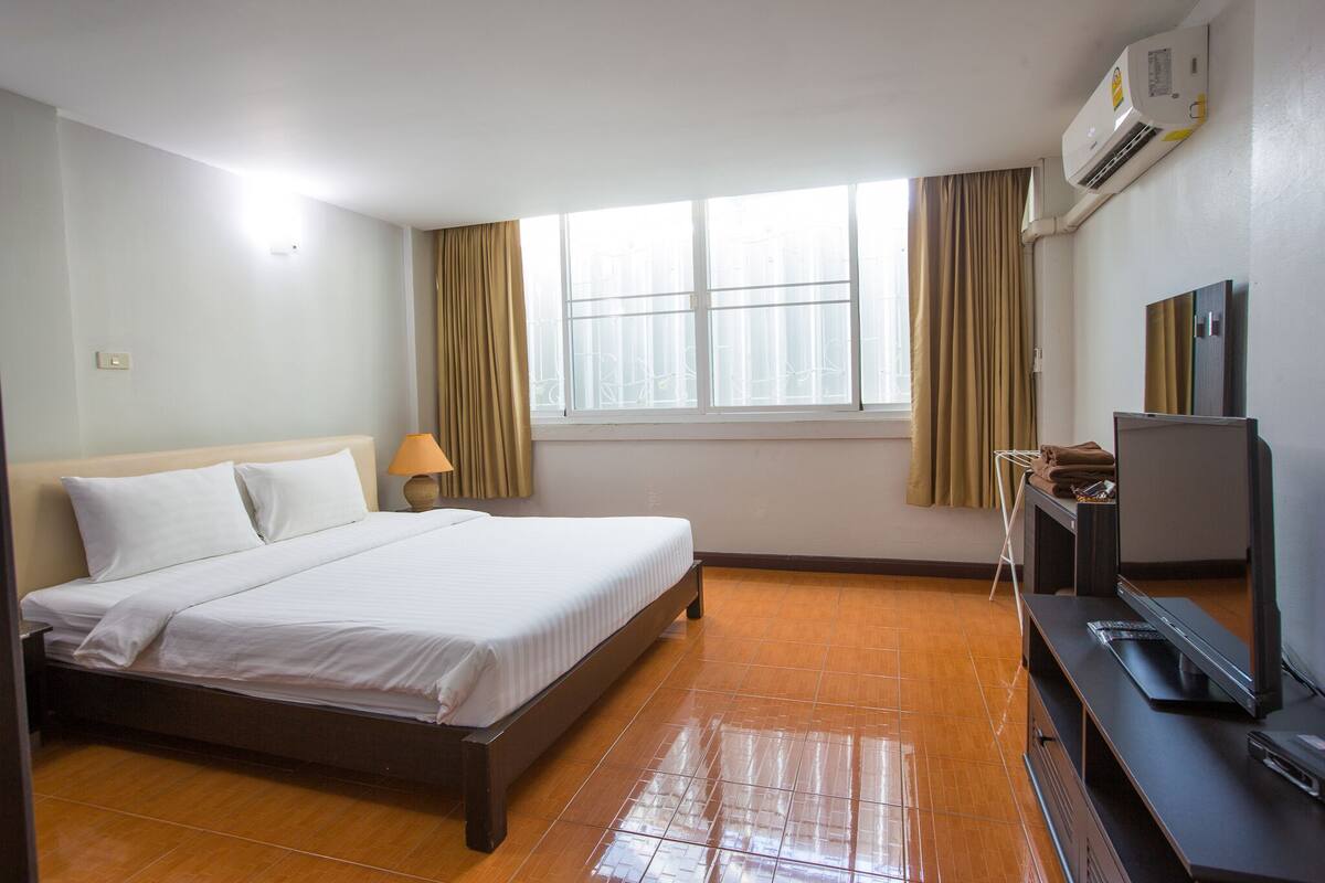 Ein Hotelzimmer mit Bett, Fernseher, Schreibtisch und einem Fenster mit Vorhängen.