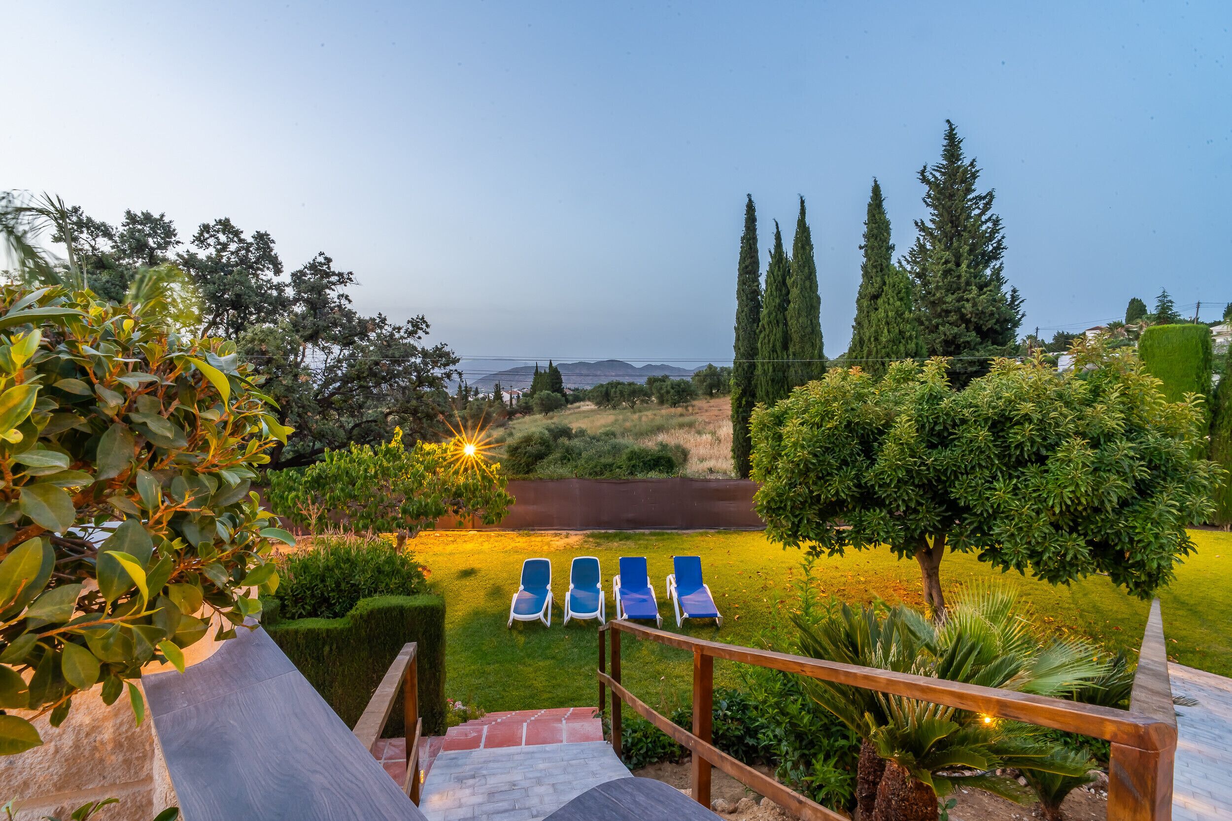 A garden with a wooden staircase, a pool with lounge chairs, and a view of the sea.
