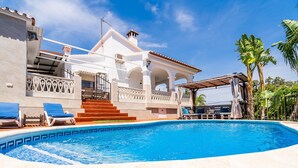 A swimming pool with a white pool deck, a covered patio area, and a staircase leading to a white building with arches and a tiled roof. - Cubo's Villa Esmeralda / private pool / garden / air conditioning / fireplace / free Wi-Fi (Alhaurín el Grande)