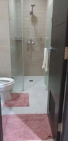 A bathroom with a glass-enclosed shower, a toilet, and a pink rug on the floor.