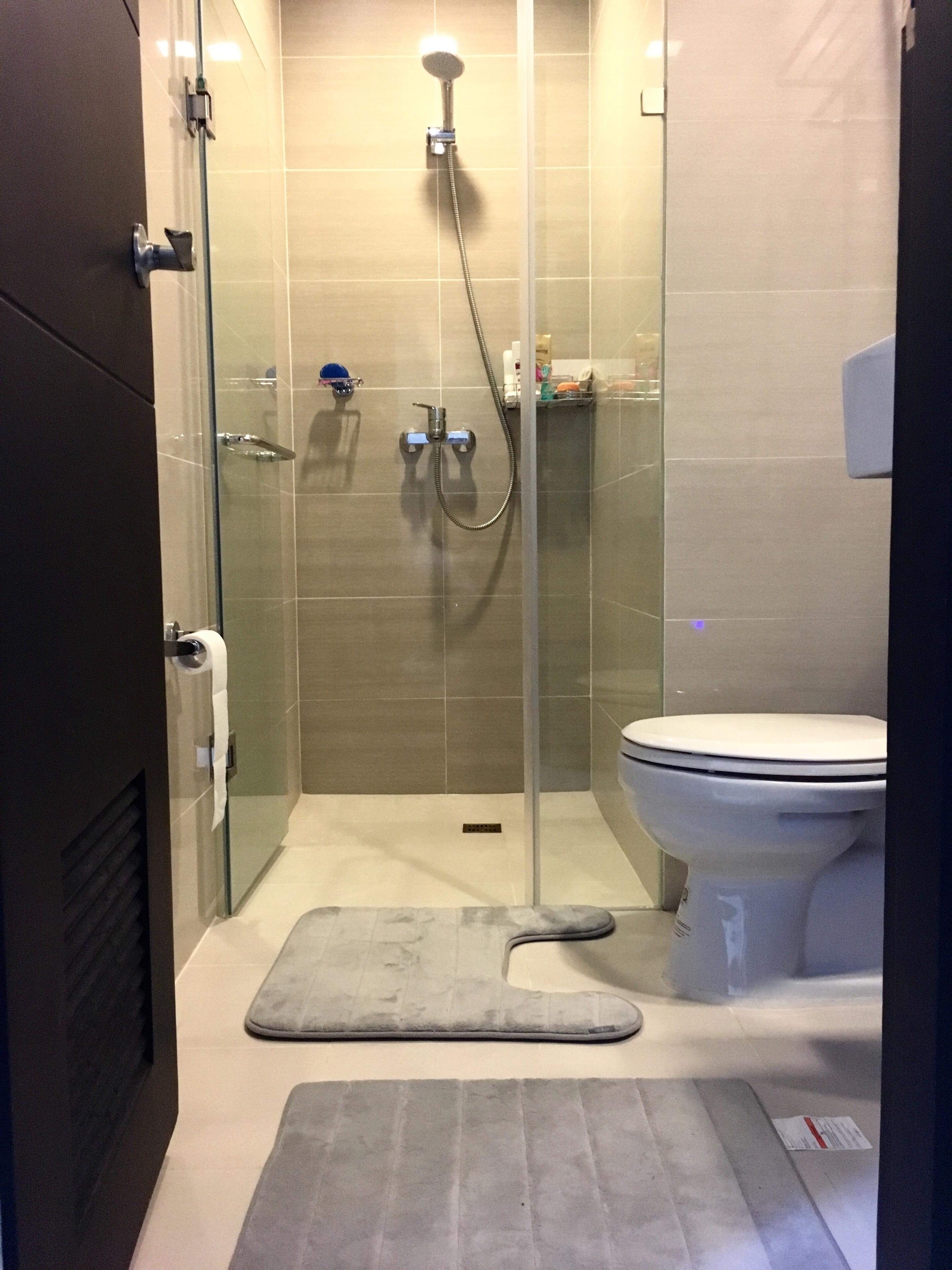A modern bathroom with a glass-enclosed shower, a toilet, and a mat on the floor.