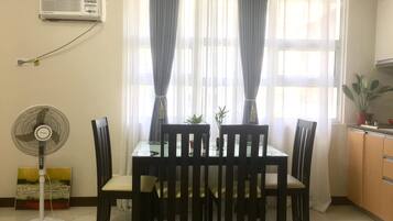 A dining area with a table, chairs, a standing fan, and a potted plant.