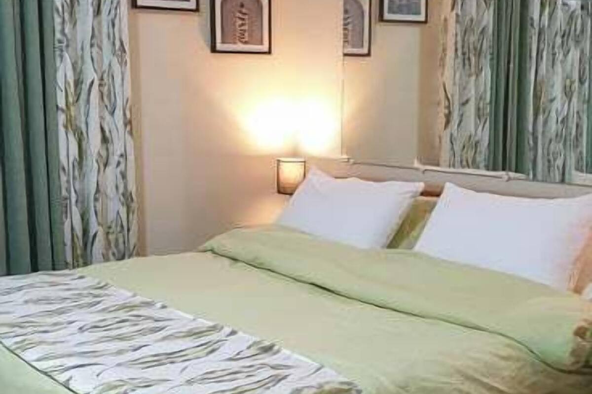A neatly made bed with a green and white floral bedspread, a wooden headboard, and a wall-mounted nightstand with a lamp.