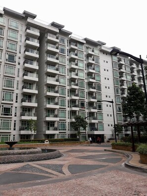 Un edificio residencial de varios pisos con balcones, un patio ajardinado y un camino peatonal.