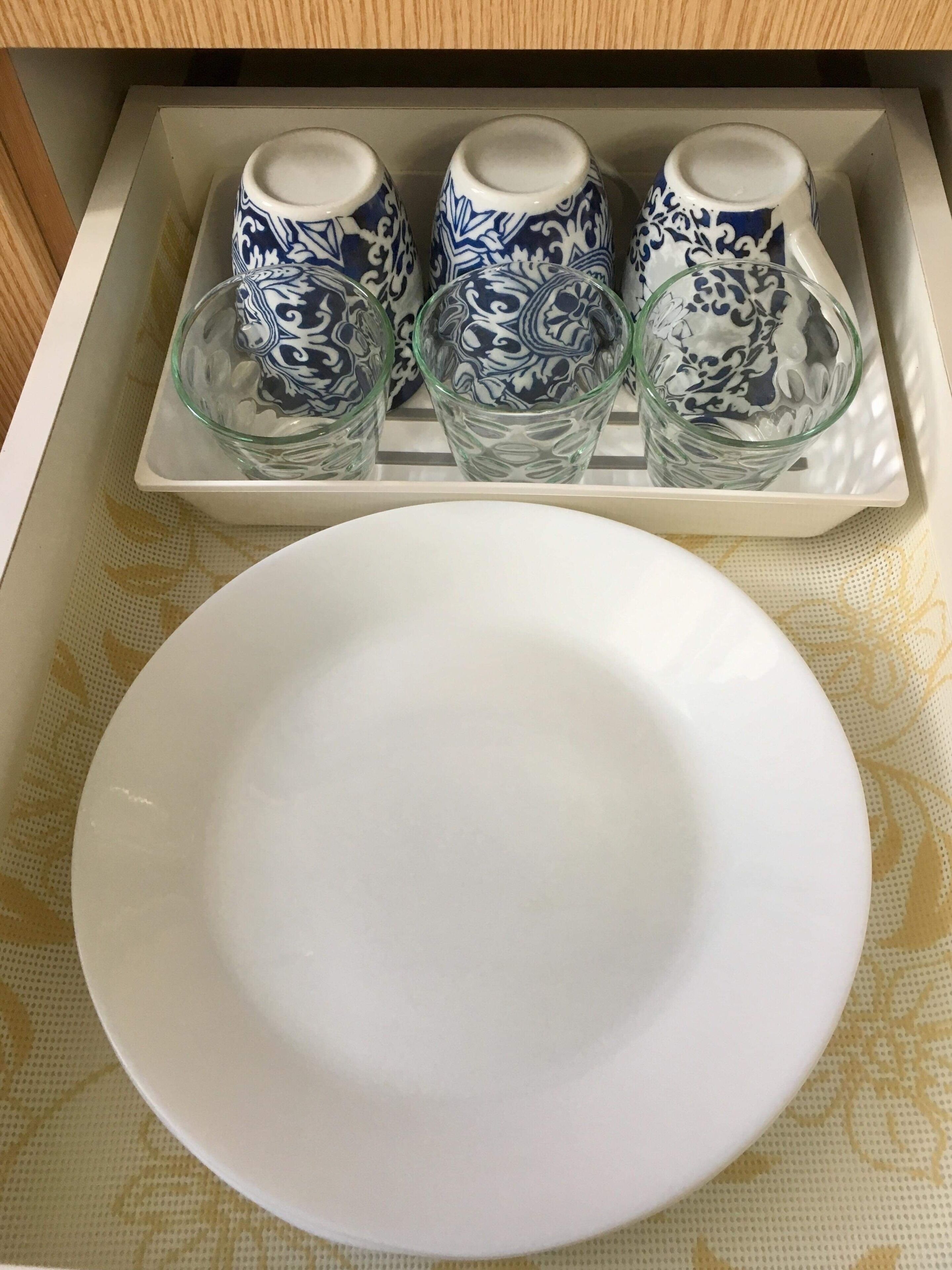 Ein Tablett mit drei verzierten Tassen und einem Glas, sowie ein weißer Teller auf einer Tischplatte.