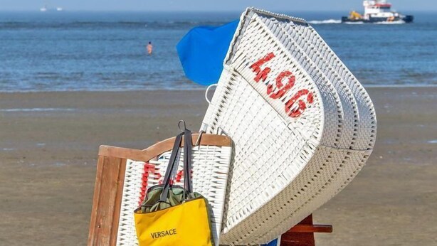 Een strandzicht met een rieten stoel, een gele tas en een houten bord.