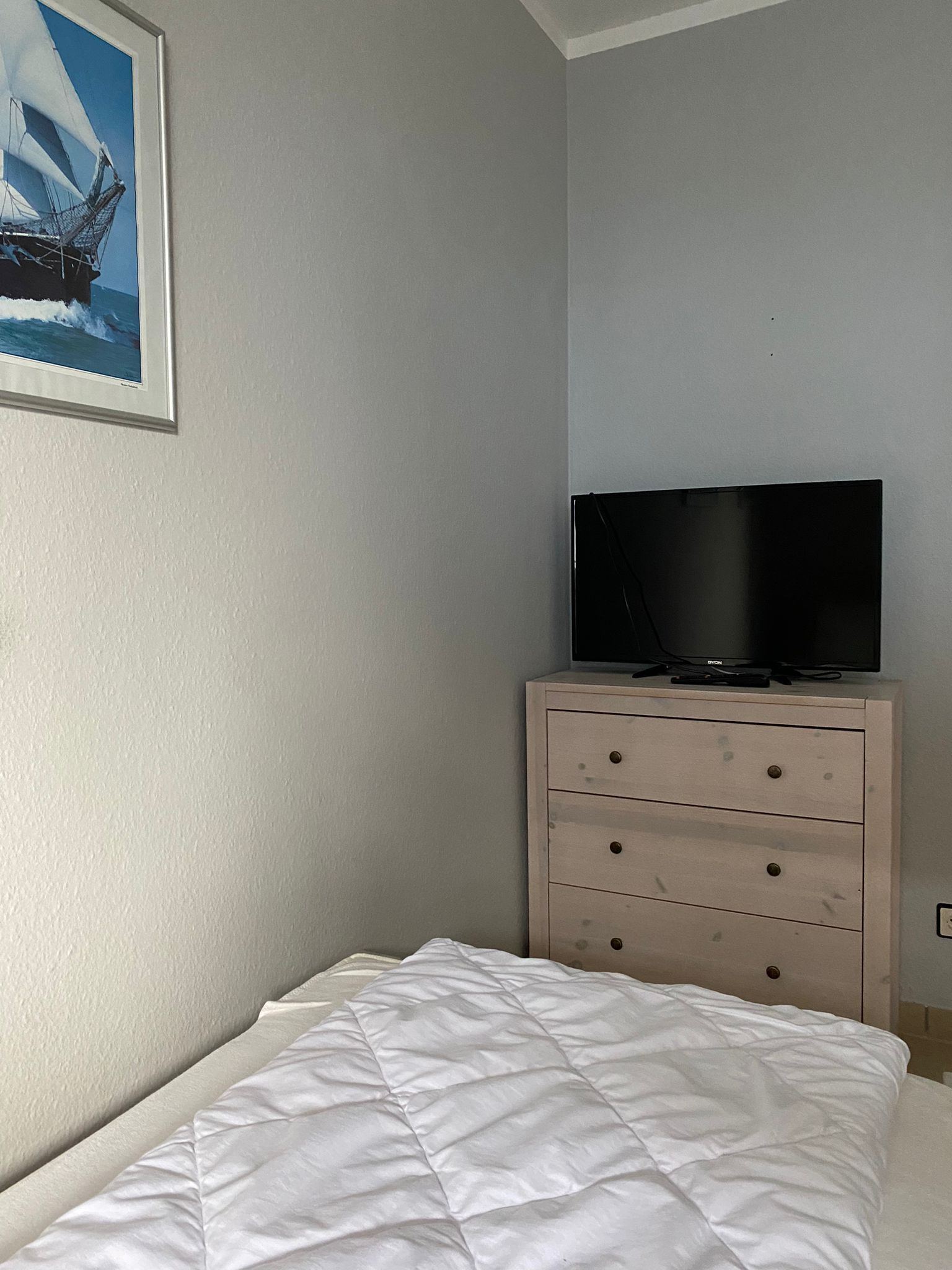 Un dormitorio con una cama, un aparador, un televisor encima del aparador y un cuadro en la pared.