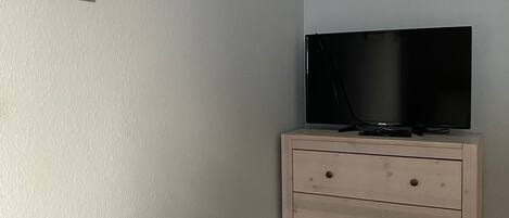 Un dormitorio con una cama, un aparador, un televisor encima del aparador y un cuadro en la pared.