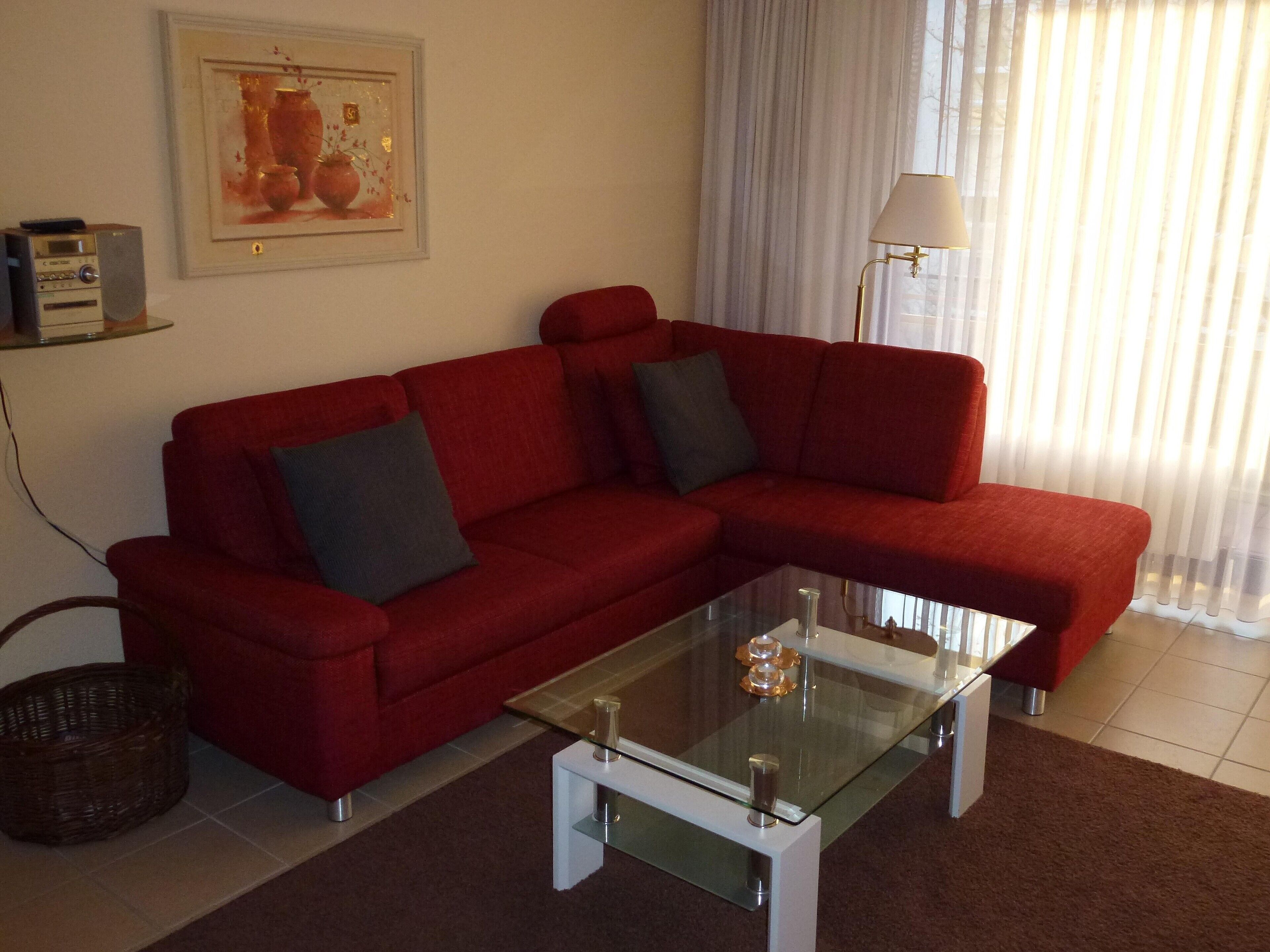 A living room with a red sofa, a glass coffee table, a lamp, a framed picture on the wall, and a basket on the floor.