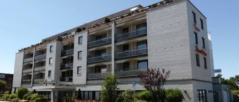 Un hotel de varios pisos con balcones, un cartel de estacionamiento y un cielo despejado.
