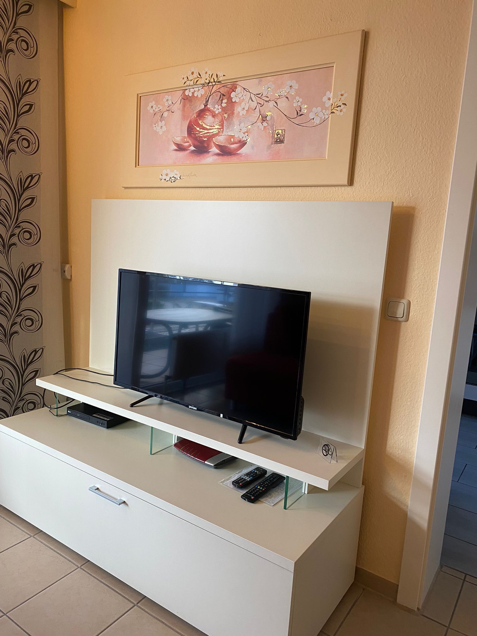 A flat-screen TV on a white entertainment unit with a remote control and a DVD player underneath.
