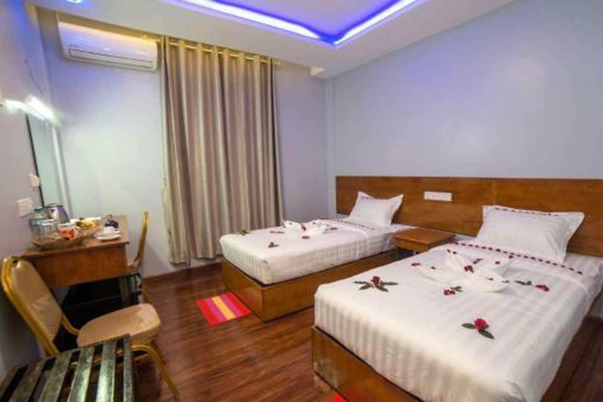 Une chambre d’hôtel avec deux lits, une tête de lit en bois, un bureau avec une chaise et une fenêtre avec des rideaux.
