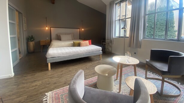 Une chambre à coucher comprenant un lit, des tables de chevet, un bureau, une chaise et une grande fenêtre.