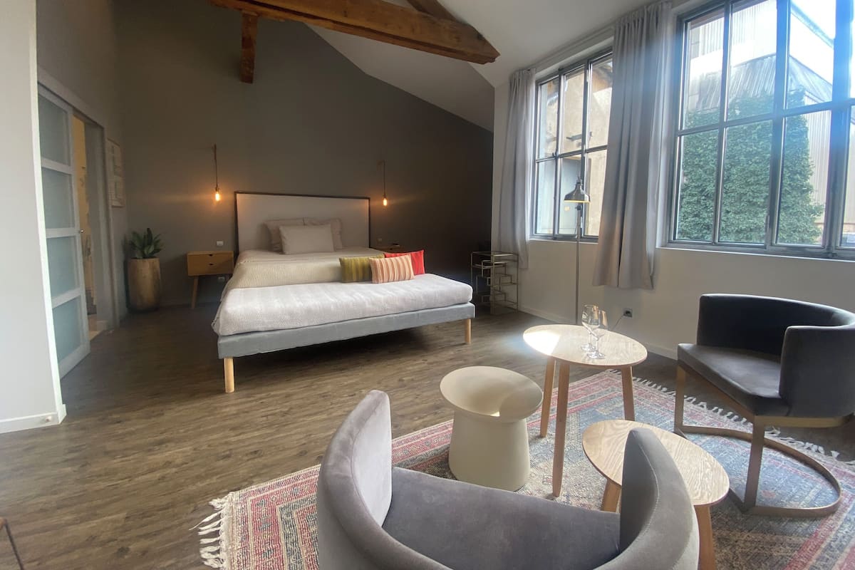 A bedroom with a bed, bedside tables, a desk, a chair, and a large window.
