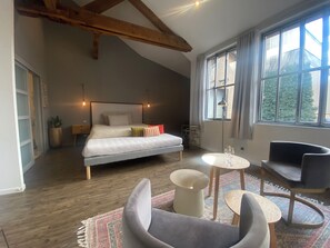 Une chambre à coucher comprenant un lit, des tables de chevet, un bureau, une chaise et une grande fenêtre.