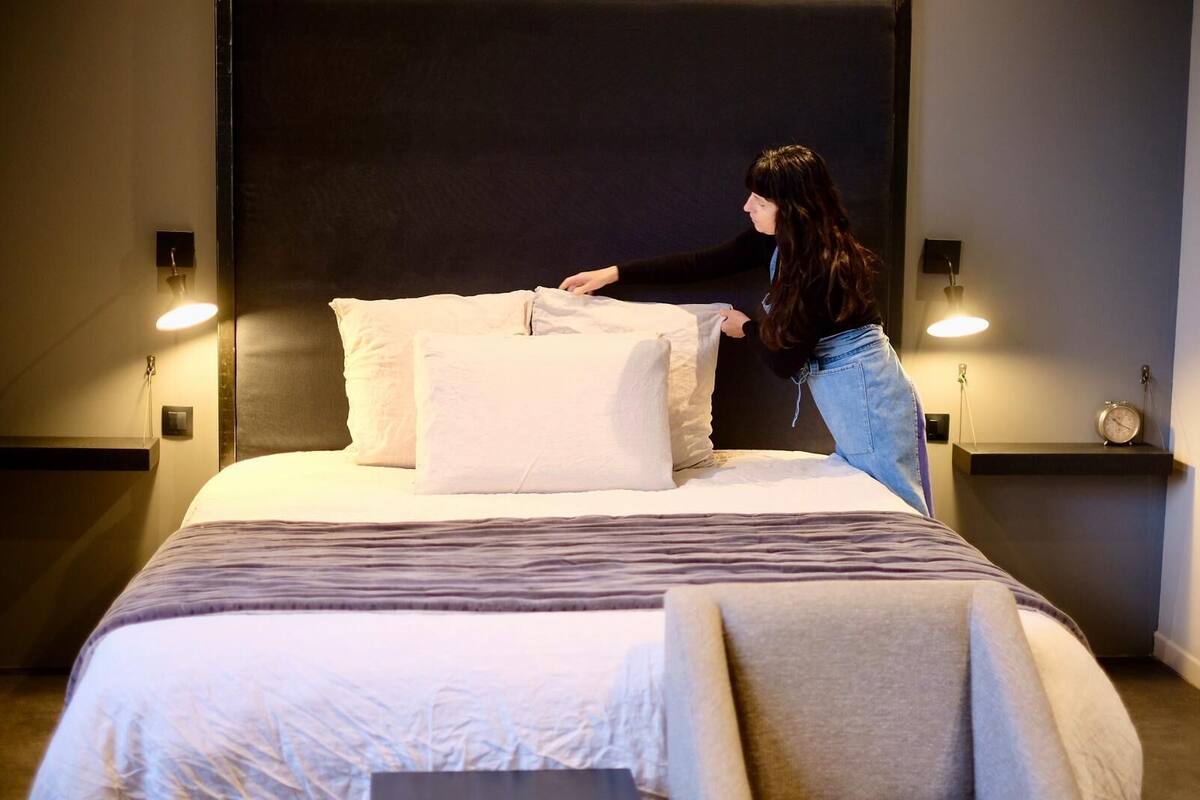 A neatly made bed with pillows and a blanket, a bedside table with a lamp, and a wall-mounted clock.
