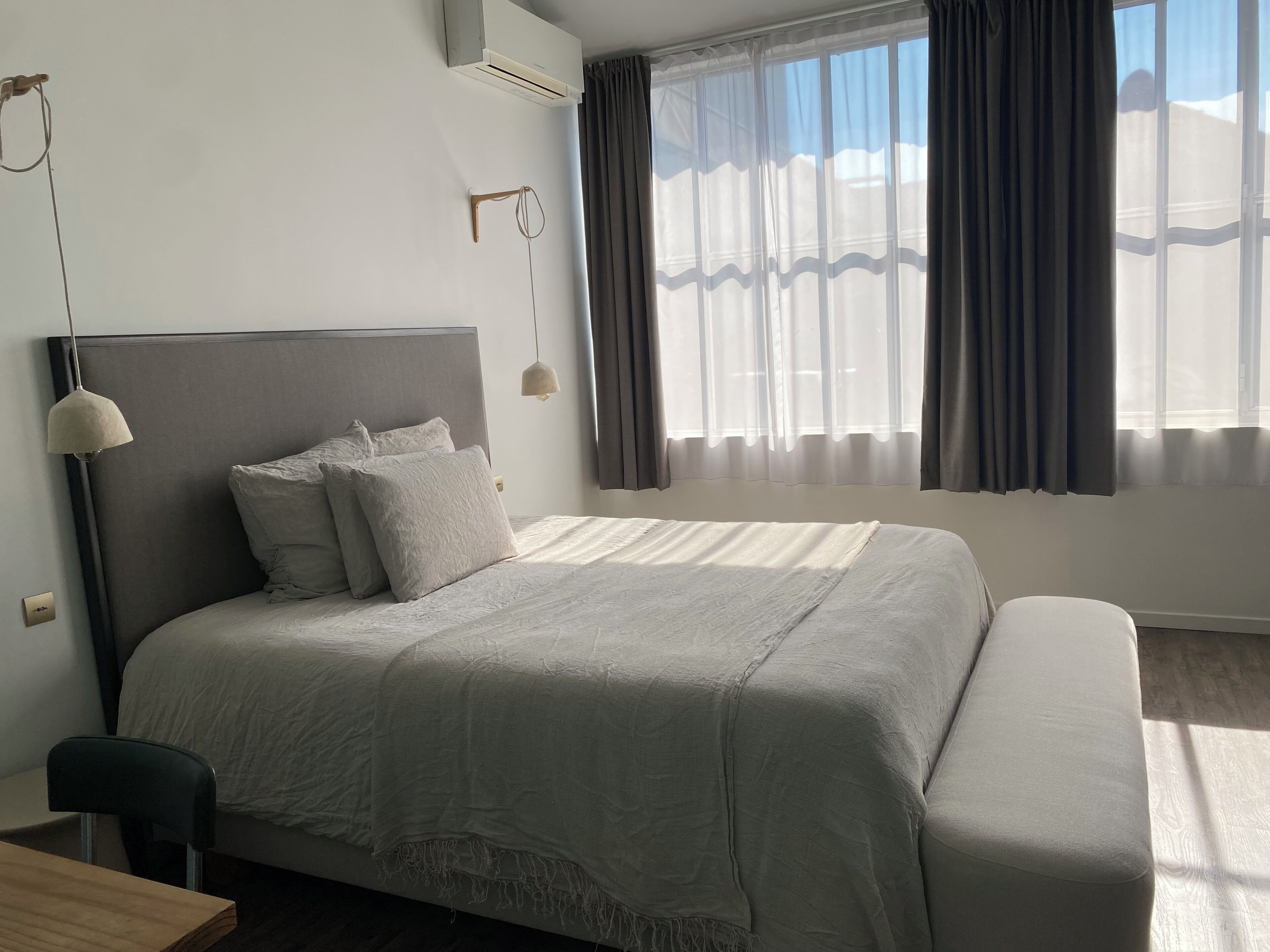 Une chambre à coucher comprenant un lit, une table de chevet, une lampe, une fenêtre avec des rideaux et un appareil de climatisation.