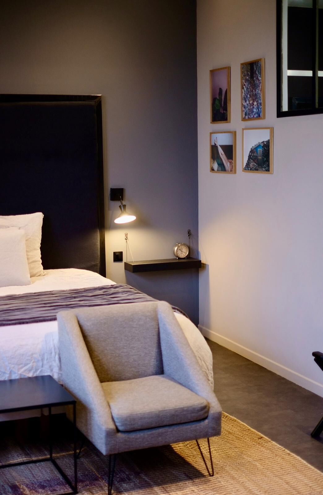 A bedroom with a bed, a chair, a nightstand with a lamp, and framed pictures on the wall.