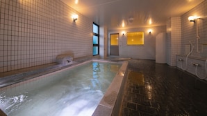 A spa area with a large hot tub, tiled walls, and a stone floor.