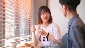 A person holding a cup at a table with a plate of food and a cup on the table.
