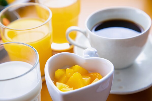Una mesa con un vaso de jugo de naranja, una taza de café y un tazón pequeño de fruta.