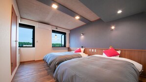 A hotel room with two beds, a window with a view, wooden flooring, and recessed ceiling lights.