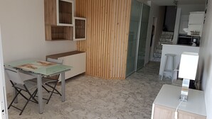 A compact kitchen with a marble floor, a wooden partition, and a small dining area with a glass table.