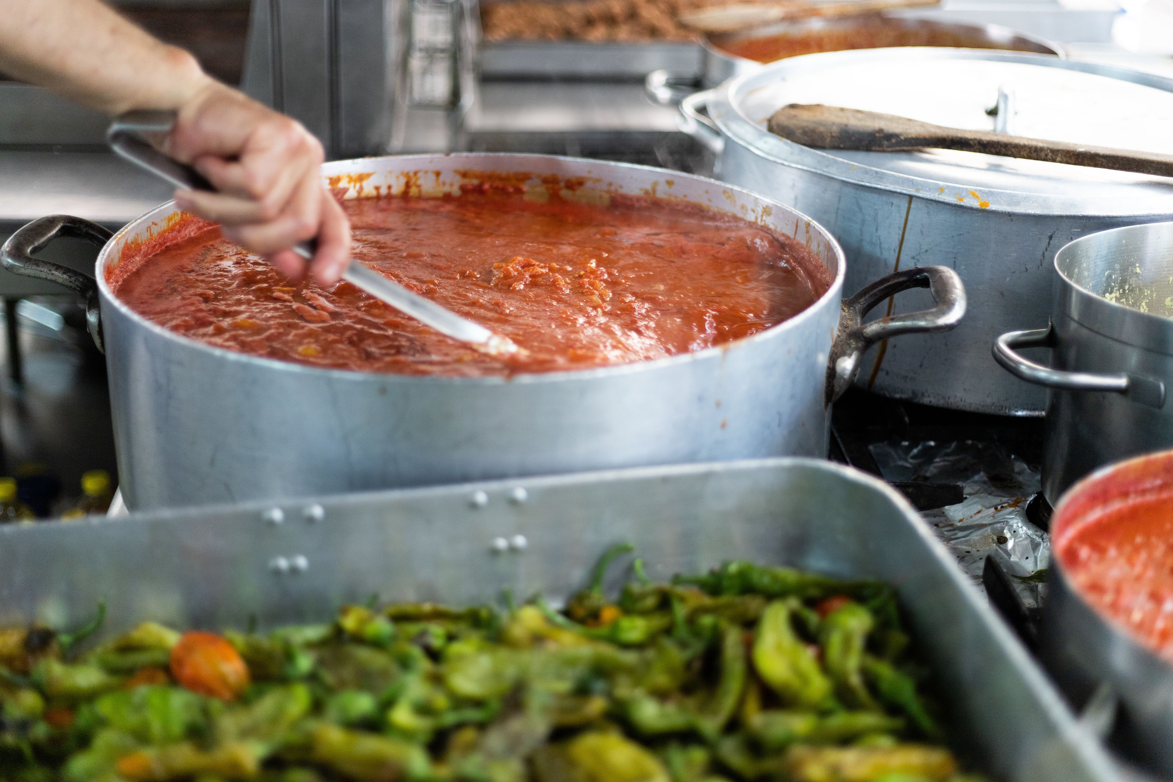 A buffet with various dishes, including a large pot of red sauce and a tray of cooked vegetables.