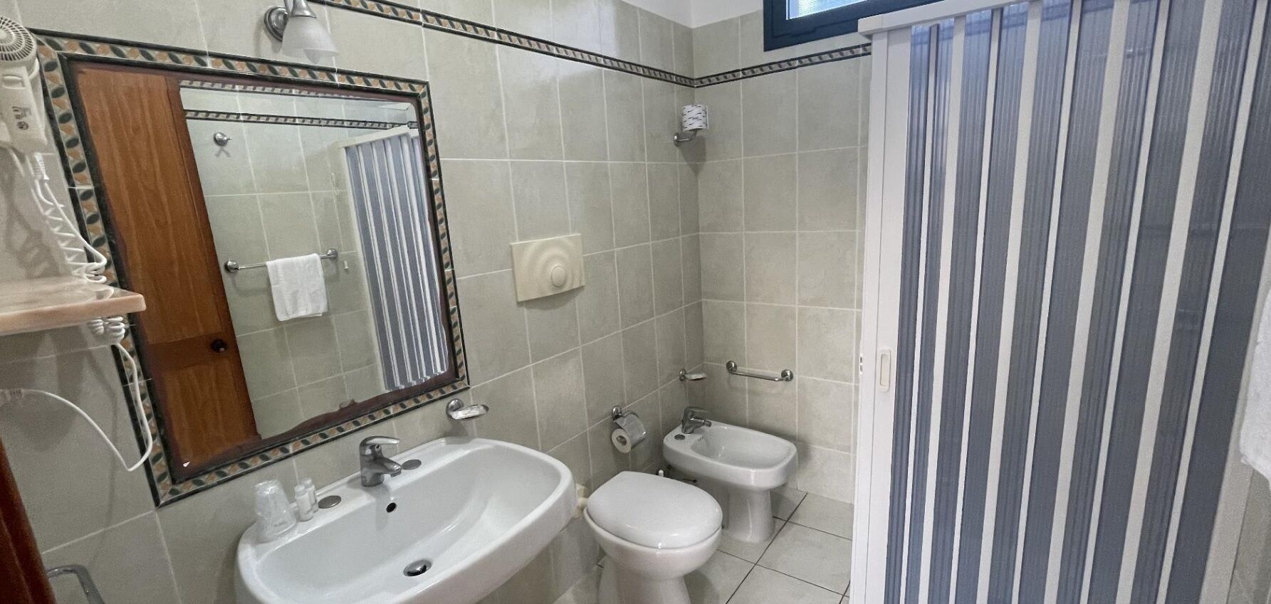 Un bany amb un lavabo, mirall, vàter, bidet i cortina de dutxa.
