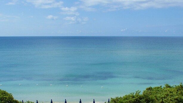 A beach with clear blue water and a line of umbrellas in the foreground. - Hotel Dei Bizantini (Manduria)