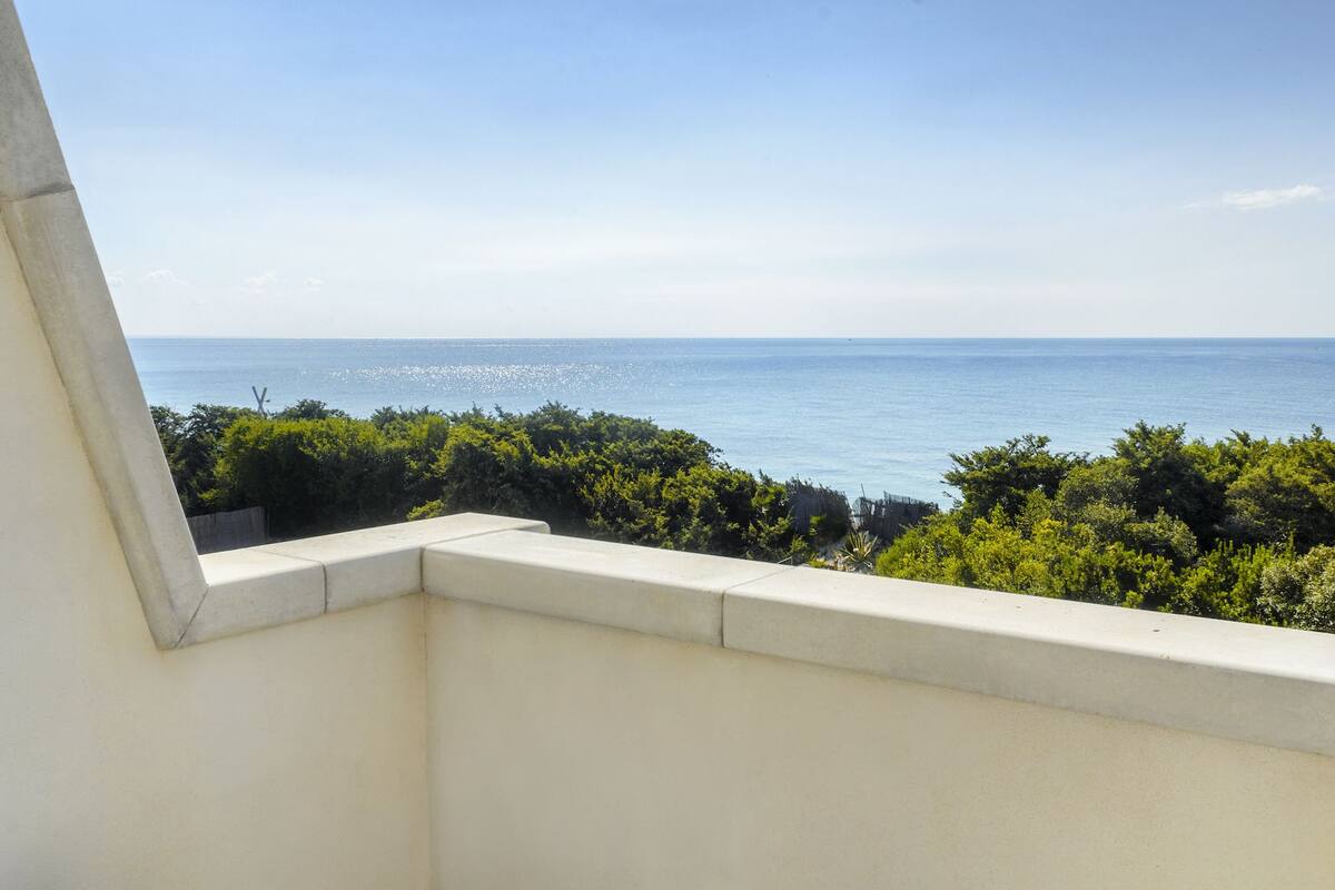 A balcony with a view of the sea and greenery.