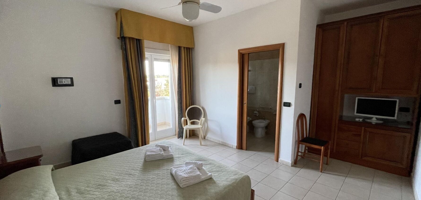 A hotel room with a bed, a chair, a television, and a bathroom visible through an open door.