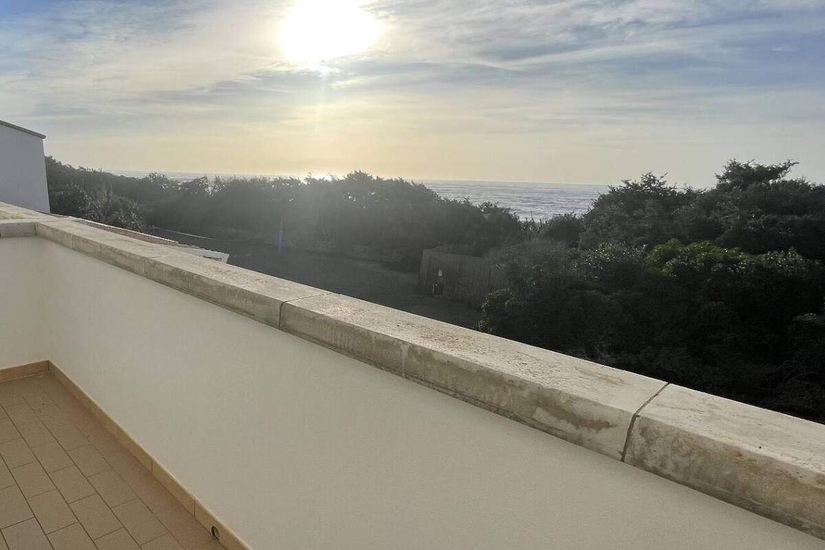 A balcony with a view of the sea and trees.