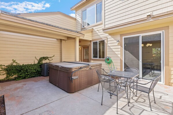 A patio with a hot tub, metal chairs, and a table.