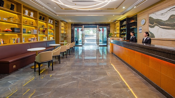 Vestíbulo de hotel con mostrador de recepción, zona de estar y estanterías con diversos artículos.