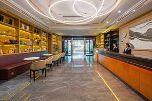 A hotel lobby with a reception desk, seating area, and shelves with various items.