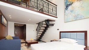 Habitación de hotel con una cama grande, un sofá azul, suelo de madera, una escalera y un cuadro en la pared.