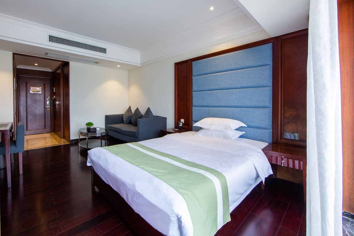 Ein Hotelzimmer mit einem großen Bett, einer Sitzecke inklusive Sofa und Sesseln, einem kleinen Beistelltisch und einem Nachttisch.