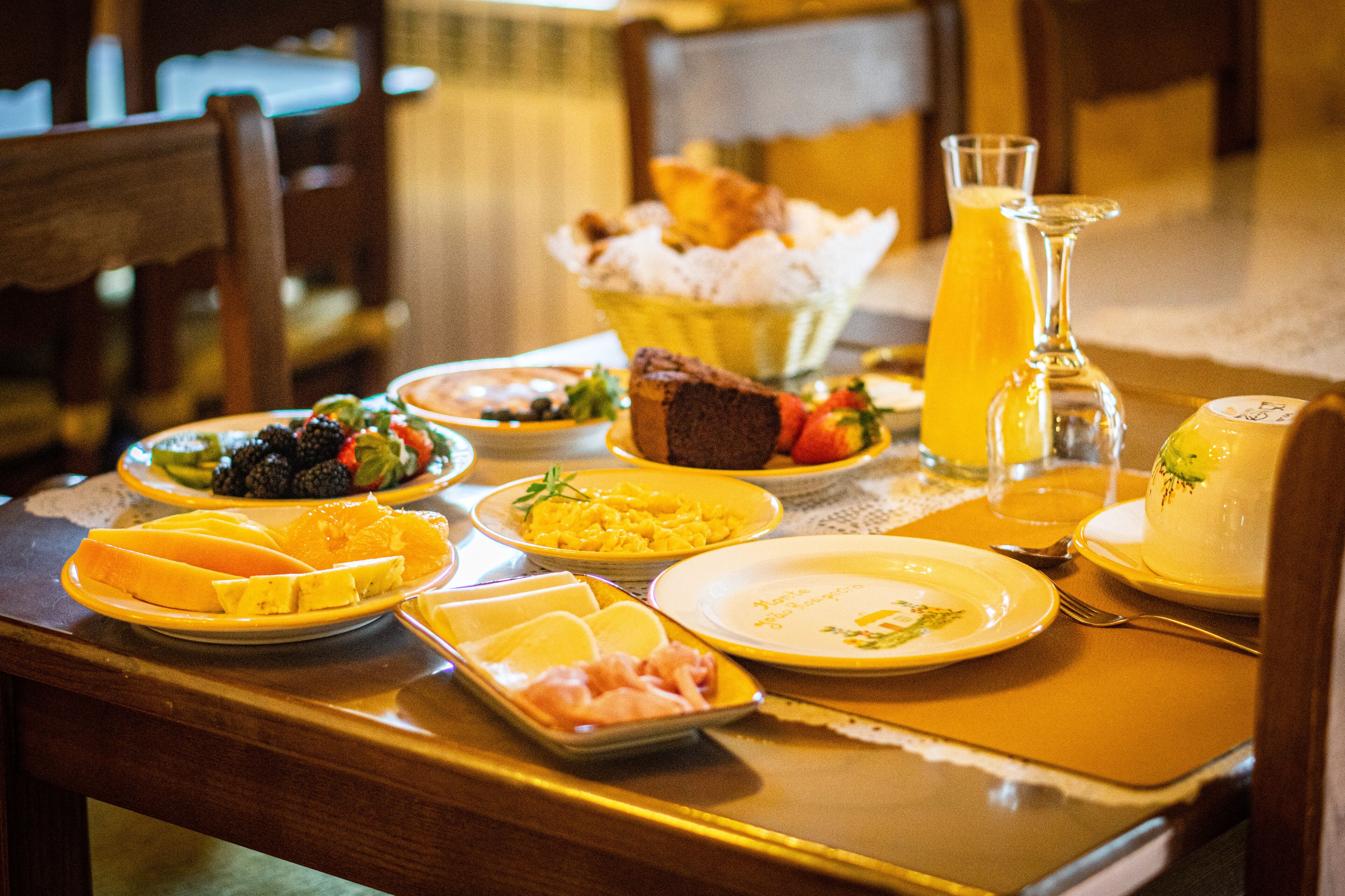 A breakfast table with various dishes, including fruits, bread, and a glass of orange juice.