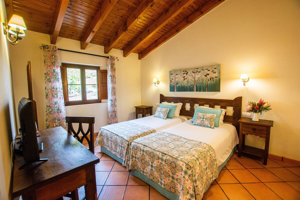 A bedroom with two beds, wooden headboards, a desk, and a chair.